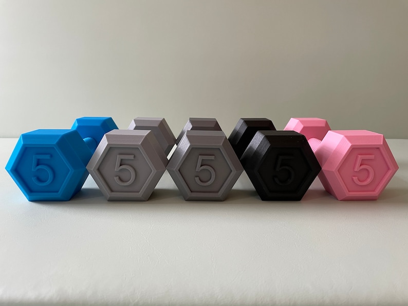 May include: Six 5-pound dumbbells in different colors: blue, gray, black, and pink. The dumbbells are arranged in a row, with the blue dumbbell on the left and the pink dumbbell on the right.