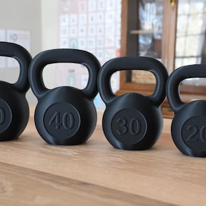 May include: Four black kettlebells with weights marked 50, 40, 30, and 20 pounds. The kettlebells are lined up in order of weight from left to right on a wooden surface.