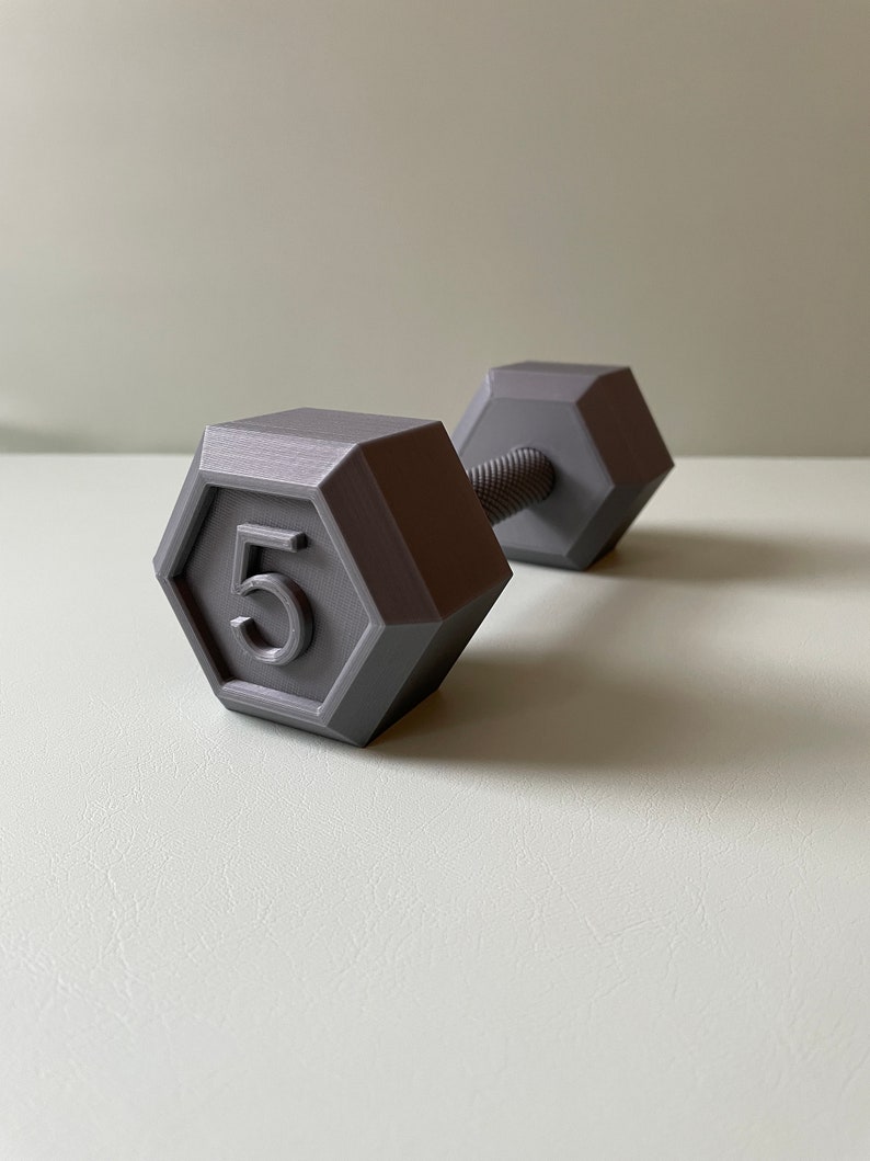 May include: A gray 5-pound dumbbell with a hexagonal shape. The dumbbell is made of plastic and has a textured surface.