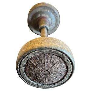 May include: Antique brass door knob with a round, sunburst design on the face. The knob has a weathered appearance, with a tarnished finish and visible wear. The design features a central circle with radiating lines.