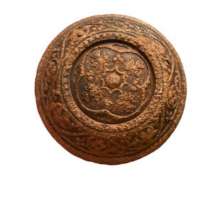 May include: A round, antique-style bronze knob with intricate floral and scrollwork patterns. The knob has a weathered appearance, suggesting age and use. The central design features a detailed floral motif.