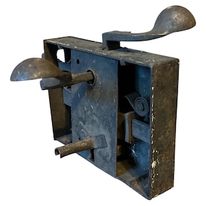 May include: An antique metal door lock, showing signs of age and wear. The lock features a lever and handle, with a rectangular body housing internal mechanisms. The metal has a dark, aged appearance, suggesting it is an antique.