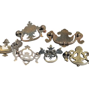 May include: A collection of six antique brass drawer pulls in various ornate designs. The pulls feature a range of shapes, including curved handles and decorative backplates, with a weathered, aged appearance. Ideal for vintage furniture restoration.