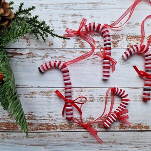 May include: Four red and white candy cane ornaments with red ribbon bows on a whitewashed wood background.