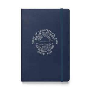 May include: A dark blue notebook with a silver embossed design. The design features the text "Corps of Engineers-U.S. Army" and a circular graphic with the text "$250 Fine or Imprisonment" and "Year 1867 Agency Rock Island District".