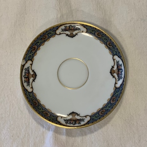 May include: A white porcelain saucer with a gold rim and a blue and green floral design. The saucer has a center well for a cup.