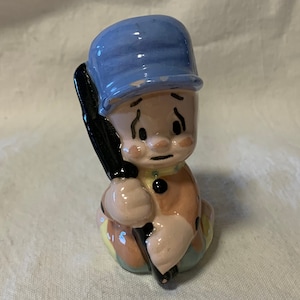 Könnte beinhalten: Eine Keramikfigur eines Jungen mit einer blauen Mütze und einem schwarzen und weißen Baseballschläger. Der Junge hat einen traurigen Gesichtsausdruck.