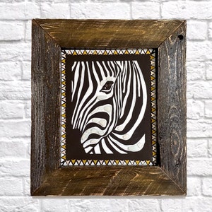 May include: A framed black and white zebra print with a geometric border in gold and white. The zebra's eye is visible in the print.
