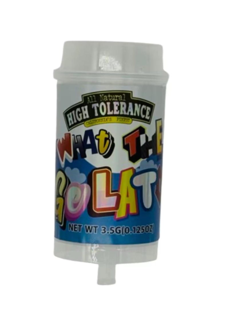 May include: A cylindrical container with a white lid and a clear bottom. The container has a label with the text "All Natural High Tolerance" and "What The Golat". The net weight is 0.125 oz.