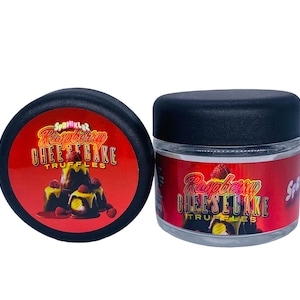May include: Two containers of Raspberry Cheesecake Truffles. One container is a black jar with a clear lid. The other container is a black lid with a red and yellow label that says "Sparkler Raspberry Cheesecake Truffles".
