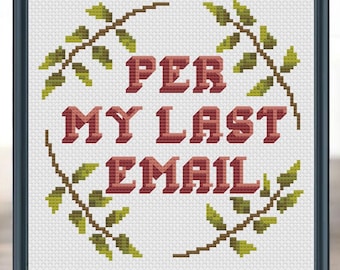 May include: Cross-stitch artwork in a black frame. The text "PER MY LAST EMAIL" is stitched in red, with a green and brown leaf border. The artwork is displayed on a wooden surface.
