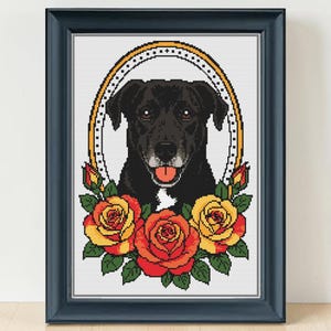 May include: A framed cross-stitch pattern featuring a black dog with a white chest patch and a pink tongue, centered within an oval border. The dog is surrounded by three large, vibrant yellow and orange roses with green leaves and stems.