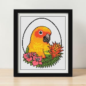 May include: Framed cross-stitch art featuring a colorful parrot with orange, yellow, and green plumage. The bird is surrounded by pink flowers, green leaves, and an orange flower, all within a black frame.