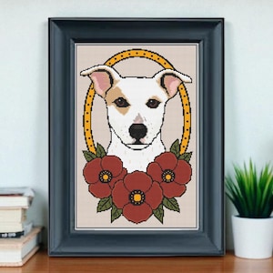 Könnte beinhalten: Gerahmtes Kreuzstich-Kunstwerk mit einem Hundepotrait in einem gelben, gepunkteten Oval, verziert mit drei roten Mohnblumen und grünen Blättern. Der Hund hat weißes Fell mit braunen Abzeichen. Der Rahmen ist dunkelblau.