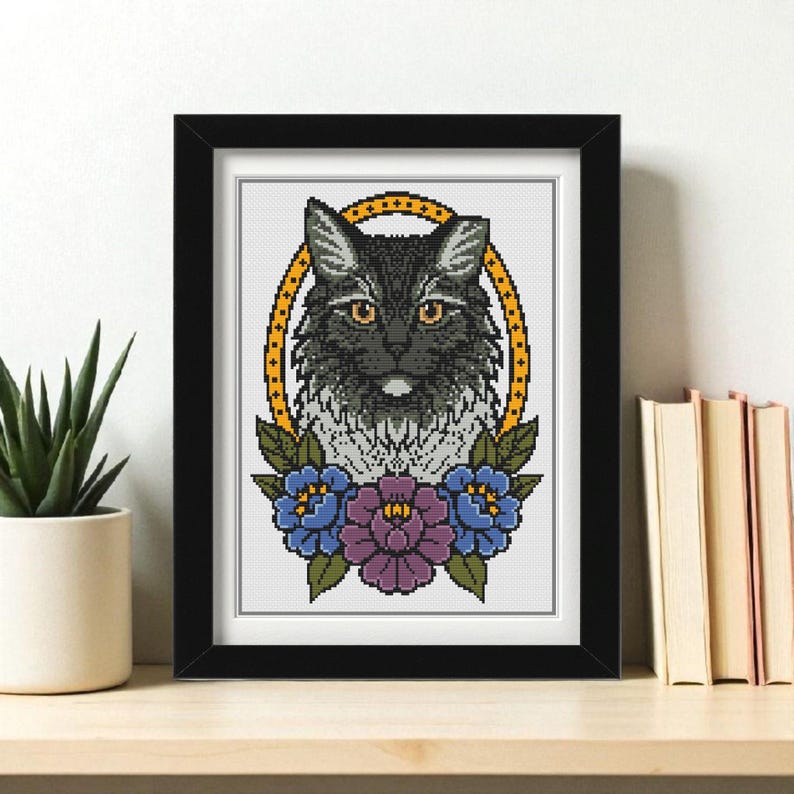 Black and white long haired cat cross stitch pattern in a floral portrait with blue and purple flowers and a gold oval frame.