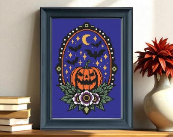 May include: Framed cross-stitch art featuring a Halloween design. The artwork showcases an orange jack-o'-lantern, bats, stars, and a crescent moon against a blue background. The frame is dark blue, and the artwork is displayed on a wooden surface.
