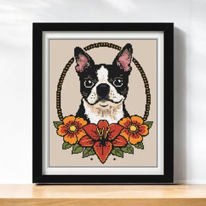 May include: Framed cross-stitch art featuring a Boston Terrier dog portrait. The dog is black and white, framed by a gold chain-like oval and surrounded by orange and red flowers. The artwork is in a black frame.