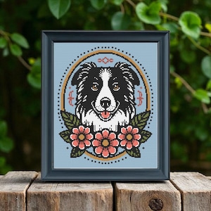 May include: A framed cross-stitch portrait of a Border Collie dog. The dog is depicted in black and white with a smiling expression. The design includes a gold-colored circular frame, pink flowers, and green leaves against a light blue background.