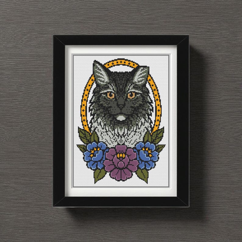 Op de afbeelding: Een ingelijste kruissteekkunst met een gedetailleerd portret van een zwarte kat met gele ogen, geplaatst in een gouden ovaal. Het ontwerp bevat blauwe en paarse bloemaccenten en is ingelijst in een zwart rechthoekig frame.