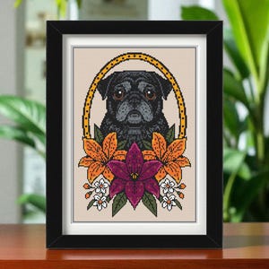 May include: Cross-stitch artwork in a black frame, depicting a black pug dog encircled by a gold oval and vibrant orange and purple flowers. The background is beige. The framed piece is displayed on a wooden surface, adding a touch of rustic charm.