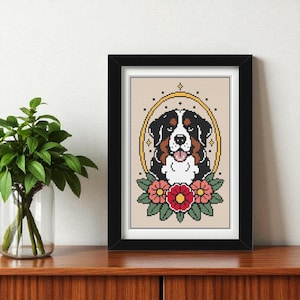 May include: Framed cross-stitch artwork of a Bernese Mountain Dog. The dog has black, white, and brown fur, set within a gold oval and floral details in red and pink. The piece is presented in a black frame, suitable for home decor.