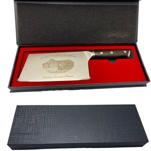 May include: A stainless steel cleaver knife with a dark wooden handle, presented in a black gift box with a red interior. The blade is engraved with a house illustration and the words "Greg and Terri Burkshare" and "Home Sweet Home."