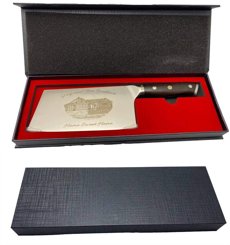 May include: A stainless steel cleaver knife with a dark wooden handle, presented in a black gift box with a red interior. The blade is engraved with a house illustration and the words "Greg and Terri Burkshare" and "Home Sweet Home."