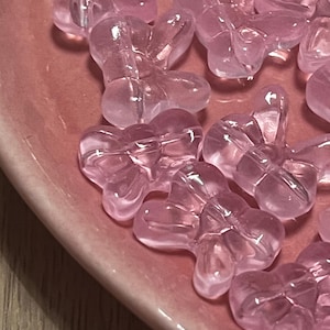 Könnte beinhalten: Nahaufnahme mehrerer durchscheinender, rosa blütenförmiger Perlen. Die Perlen sind auf einem rosa Keramikteller angeordnet. Die Perlen haben eine glänzende Oberfläche und sind gleichmäßig verteilt.