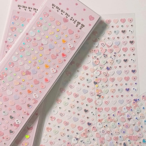 Può includere: Adesivi rosa a forma di cuore con dettagli olografici. Gli adesivi sono disposti su uno sfondo rosa chiaro e sono confezionati in plastica trasparente. Il testo sulla confezione è in coreano.