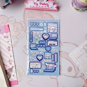 May include: A sheet of blue and white stickers featuring a cartoon dog with a pink heart. The stickers are in a clear plastic sleeve with a pink header that says "My Melody".
