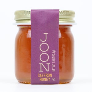Peut inclure: Un pot en verre de miel au safran avec une étiquette violette sur laquelle est inscrit "NOON" et "SAFFRON HONEY". L'étiquette comprend également le texte "NET WT 1.5 OZ (42.5g)".
