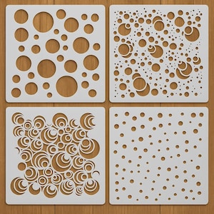 May include: Four white square stencils featuring different circular cut-out designs. The patterns include random circles, overlapping circles, and a design of small dots. The stencils are displayed on a wooden surface.