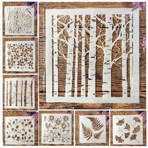 Könnte beinhalten: Eine Sammlung weißer Kunststoffschablonen mit verschiedenen von der Natur inspirierten Designs. Die Schablonen umfassen Baumrinde, Blumenmuster, Birken, Farne und Ginkgoblätter. Diese Schablonen sind ideal für Bastel- und Dekorationsprojekte.