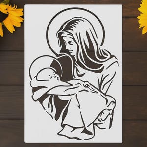 May include: A stencil featuring a religious image of a woman holding a child. The woman is depicted with a halo, and the image is rendered in a simple, two-tone style, suitable for various craft projects.