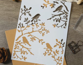 May include: A white card with a cut-out design of birds perched on tree branches. The branches and birds are a light brown color. The card is on top of a brown envelope.