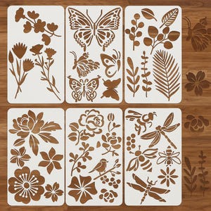 Może przedstawiać: Zestaw szablonów z różnymi wzorami inspirowanymi naturą. Szablony zawierają wzory kwiatowe, motyle, pszczoły, ważki i elementy botaniczne. Szablony są białe z brązowymi wycięciami, idealne do rękodzieła i projektów DIY.