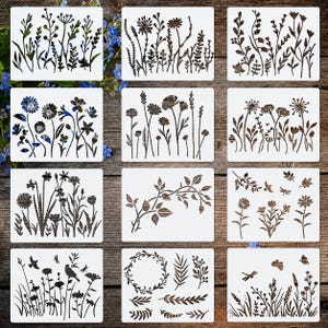 Puede incluir: Nueve plantillas blancas con diversos diseños florales y botánicos. Cada plantilla presenta una disposición diferente de flores, hojas y tallos en color marrón oscuro. Las plantillas están dispuestas sobre una superficie de madera.