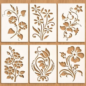 Puede incluir: Seis plantillas florales blancas con varios diseños de flores y hojas. Cada plantilla es rectangular y presenta un patrón botánico diferente, recortado para revelar la veta de la madera debajo. Ideal para manualidades y proyectos decorativos.