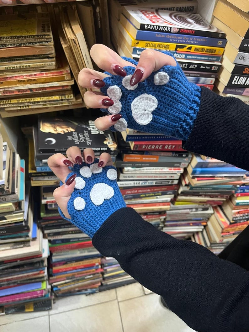 Pu&ograve; includere: Un paio di guanti senza dita blu con impronte di zampe bianche. I guanti sono all'uncinetto e hanno un polsino nero.