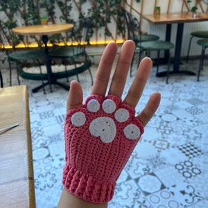 May include: Pink crocheted fingerless gloves with a white paw print design.
