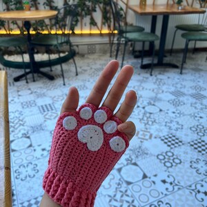 May include: Pink crocheted fingerless gloves with a white paw print design.