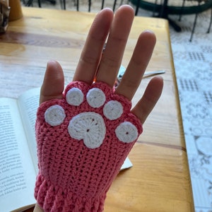 May include: Pink crocheted fingerless gloves with a white paw print design.