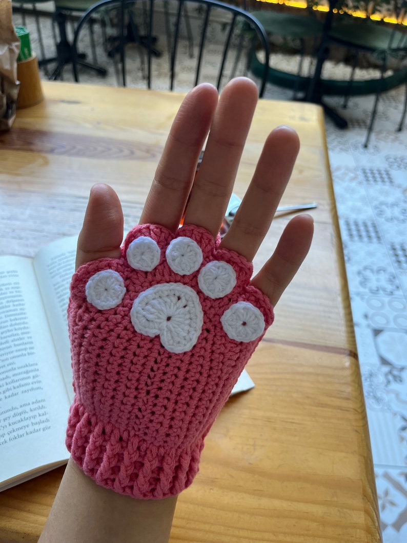May include: Pink crocheted fingerless gloves with a white paw print design.