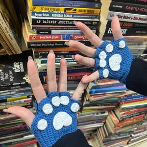 Pu&ograve; includere: Un paio di guanti senza dita blu con impronte di zampe bianche. I guanti sono all'uncinetto e hanno un aspetto testurizzato.