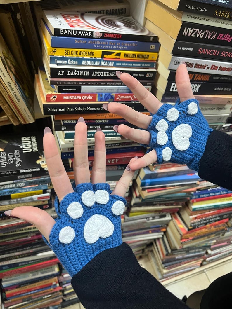 Pu&ograve; includere: Un paio di guanti senza dita blu con impronte di zampe bianche. I guanti sono all'uncinetto e hanno un aspetto testurizzato.