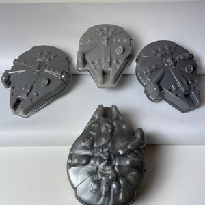 May include: Four grey plastic moulds shaped like the Millennium Falcon spaceship from Star Wars. The moulds are on a white surface.