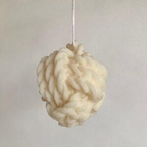 Könnte beinhalten: Eine weiße, strukturierte Kerze in Kugelform, die an einer weißen Schnur hängt.