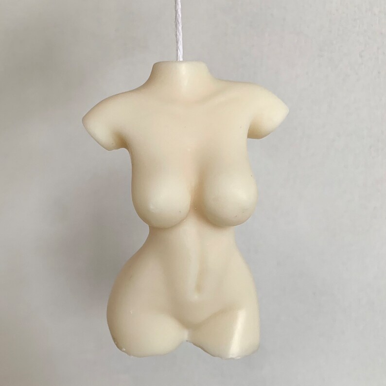May include: A white candle shaped like a human torso. The candle is hanging from a white string.