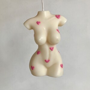 May include: A white candle shaped like a human torso with pink hearts on the surface.