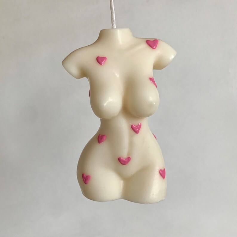 May include: A white candle shaped like a human torso with pink hearts on the surface.